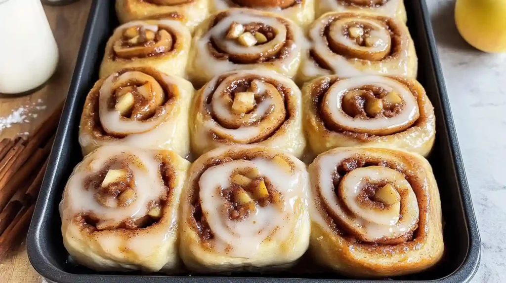 Baking pan of apple cinnamon rolls topped with vanilla glaze.