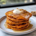 Fluffy sweet potato pancakes stacked on a plate with maple syrup, warm fall spices, and a golden, bakery‑soft crumb.